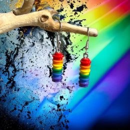 A pair of lego studs in colours of the rainbow stuck together to make a column hanging off hook earrings with a rainbow background.