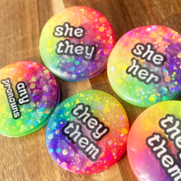 Glow in the dark rainbow pronoun badges with she/they, they/them, and any pronoun labels. Handmade in Melbourne by iridian.design.
