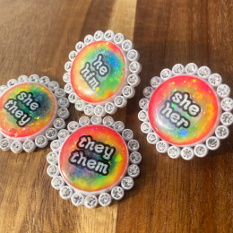 Four white rhinestone glowing rainbow pronoun pins with she/her, they/them and he/him labels. Handmade in Melbourne by iridian.design.
